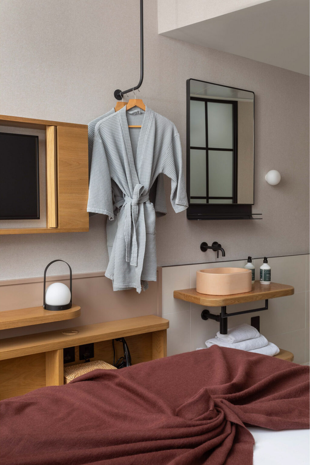 hotel bedroom with burgundy blanket and two robes hanging up