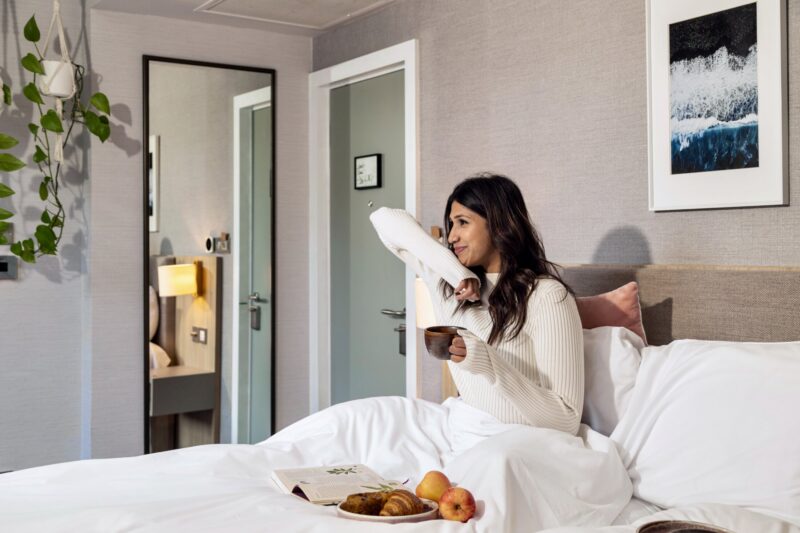 Guest sat in bed eating breakfast and drinking coffee at Inhabit Queen's Gardens